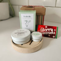 Two small containers of cream on a wooden tray with a Frabilla skincare product box and a Christmas-themed card in the background.